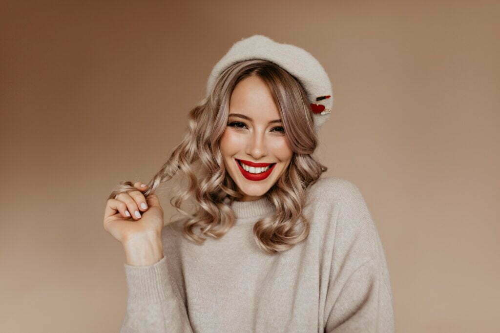 Appealing french lady playing with her long hair. Wonderful white girl in brown beret smiling to camera.