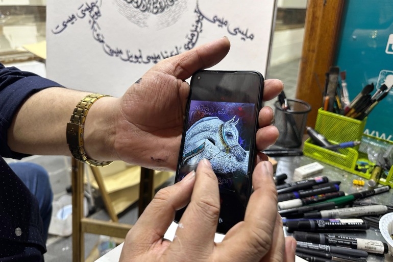 Mâinile lui Khaled Almesawy țin un iPhone cu o imagine a unui cal alb pe el.  Șevaletul care arată partea inferioară a schiței lui Messi se află în spatele mâinilor sale, alături de pensule și creioane.  Purtați un ceas placat cu aur..