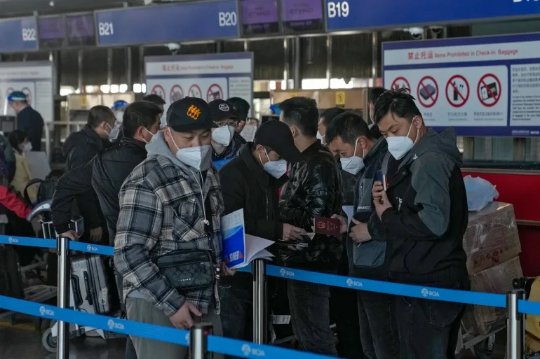 Călătorii mascați își verifică pașapoartele în timp ce se aliniază joi la ghișeul de check-in al zborurilor internaționale de pe Aeroportul Internațional Beijing Capital