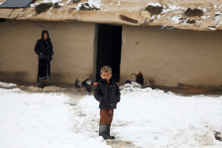 Un băiat afgan stă pe pământ înzăpezit în Kabul
