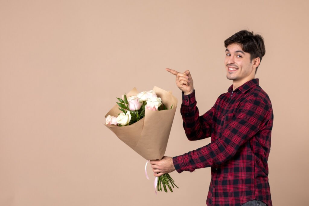 front-view-young-male-giving-beautiful-flowers-brown-wall